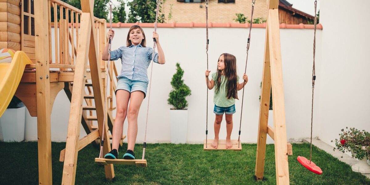 Espace de jeu pour enfants dans un jardin familial avec balançoire et petite cabane en bois.