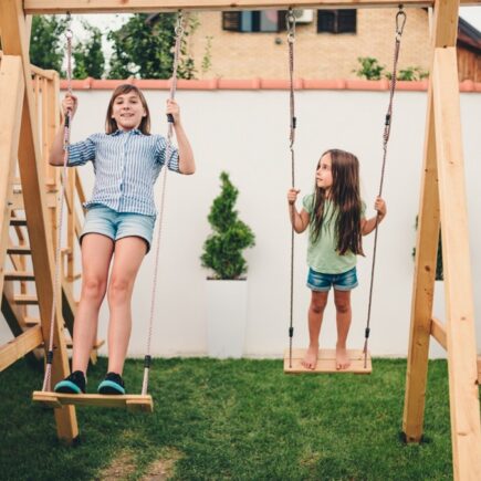 Espace de jeu pour enfants dans un jardin familial avec balançoire et petite cabane en bois.