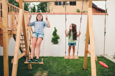 Espace de jeu pour enfants dans un jardin familial avec balançoire et petite cabane en bois.