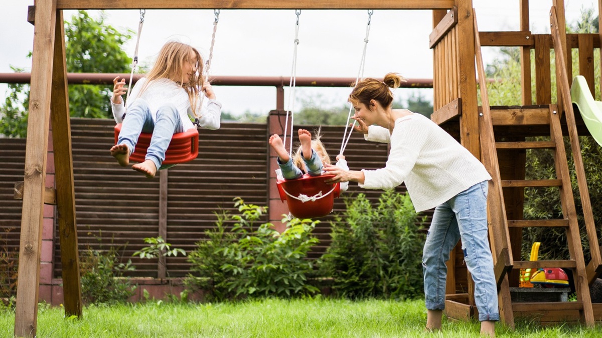 Enfants jouant dans un jardin aménagé avec jeux d’extérieur, sol sécurisé et espace délimité.