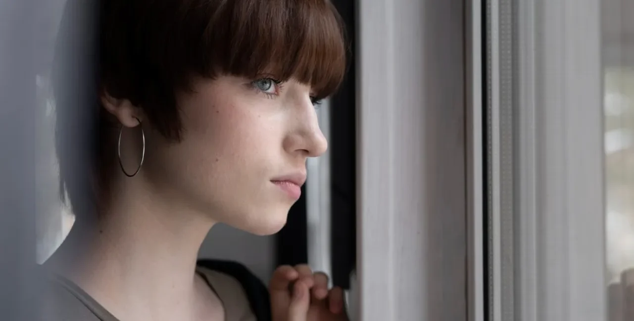Personne pensive près d’une fenêtre illustrant les signes invisibles du traumatisme